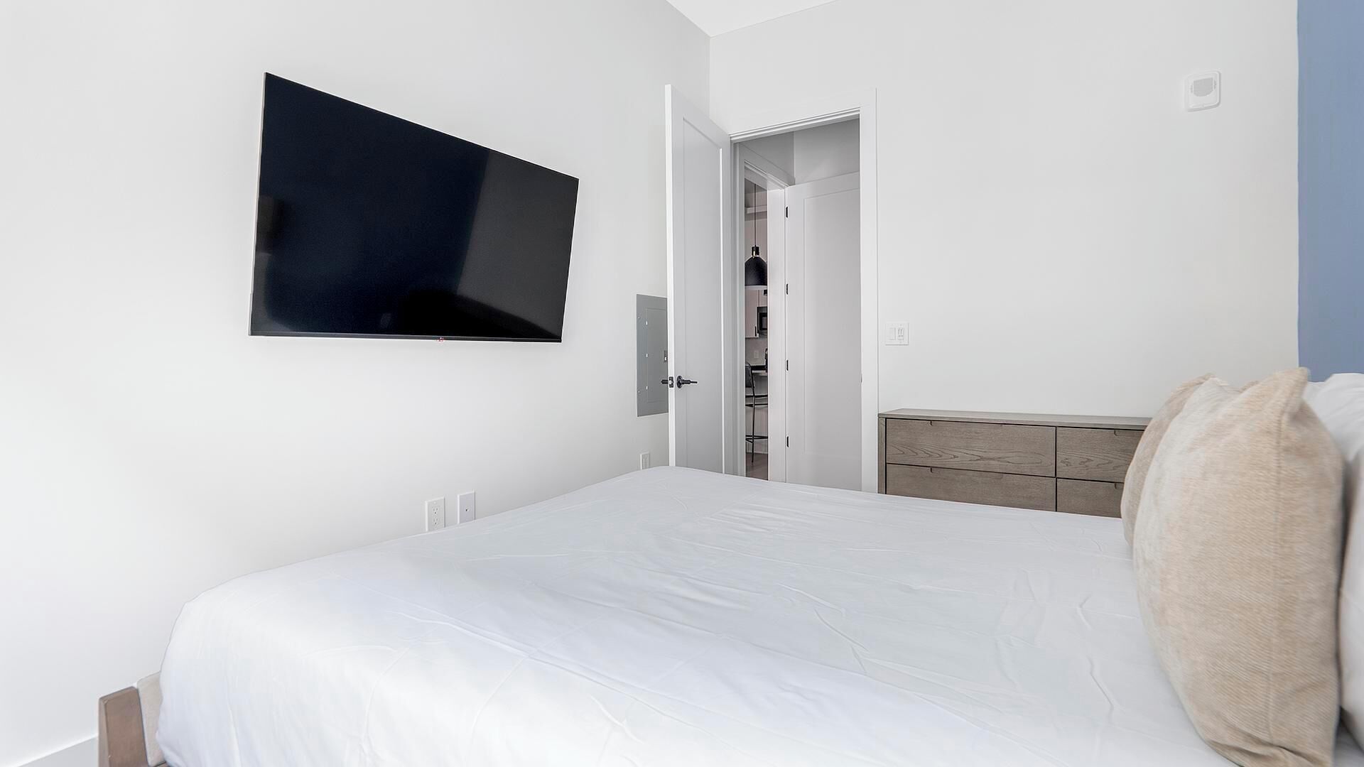 Een moderne slaapkamer met een groot bed, een flatscreen televisie aan de muur en een kledingkast met een houten hoofdbord.