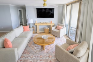 Una sala de estar con sofá, sillón, mesa de centro y televisor de pantalla plana montado en la pared.