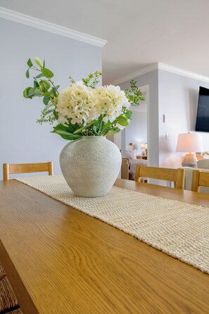Una mesa de comedor con un tapete texturizado, un florero de piedra con flores blancas y sillas de madera.