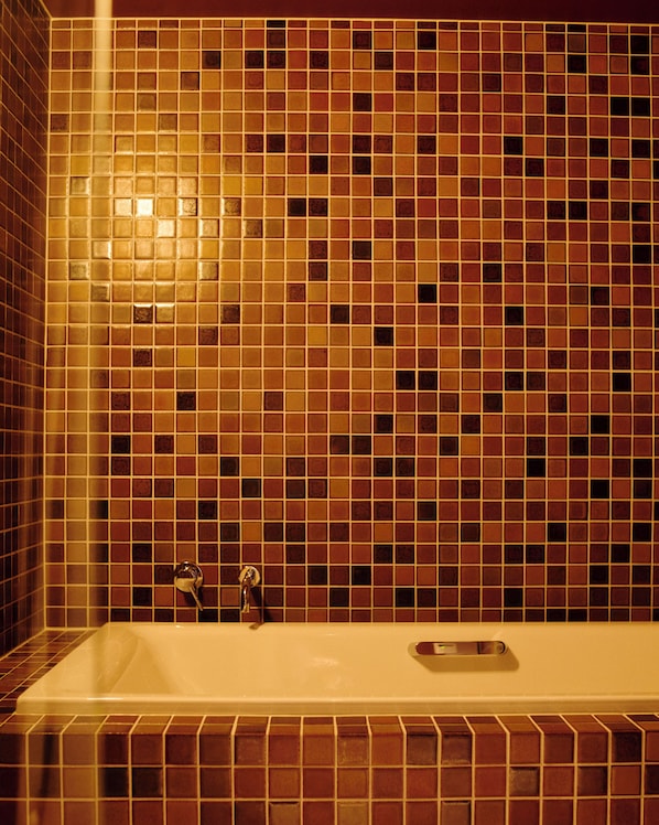 Un baño con pared de azulejos y una bañera.