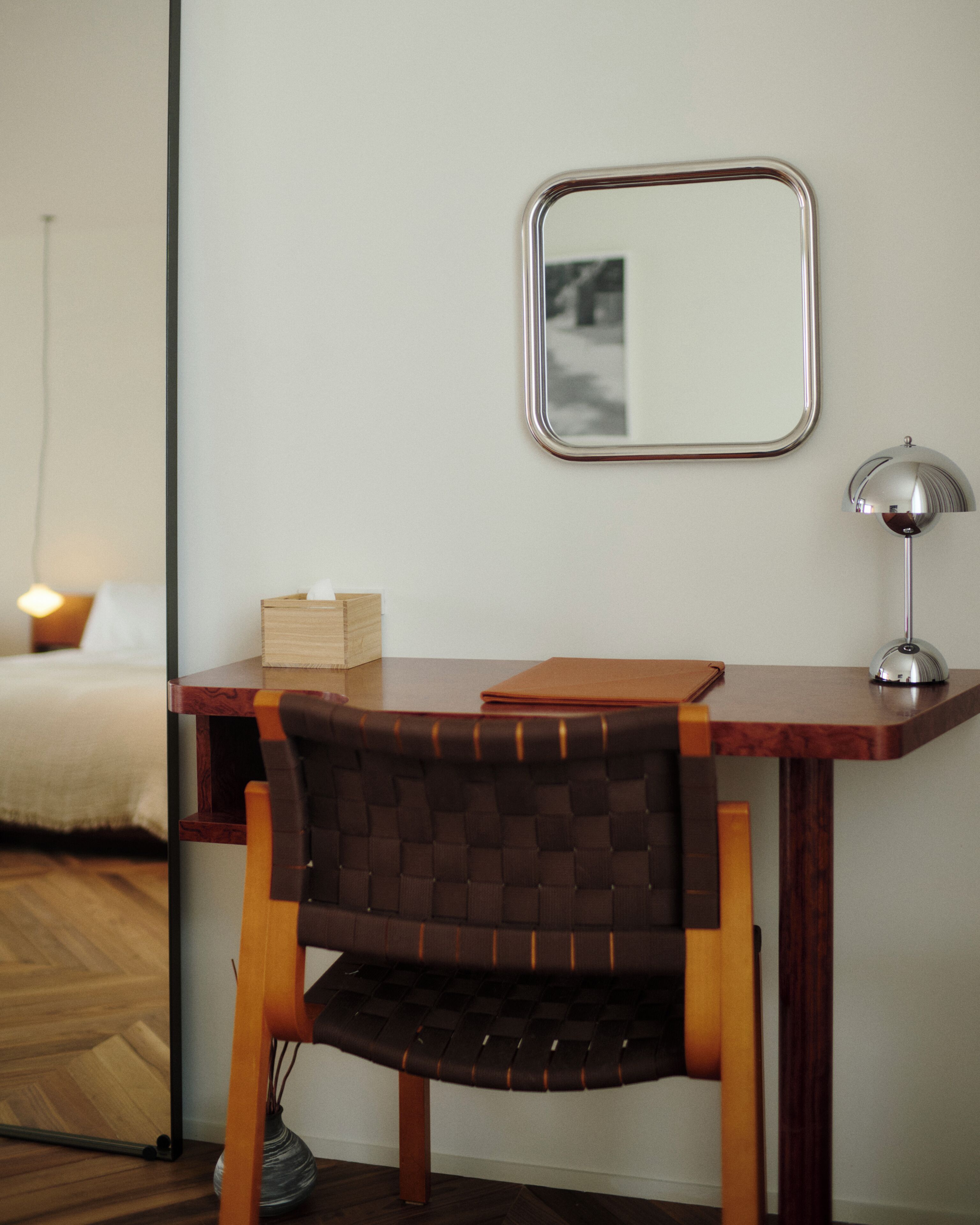 A wooden desk with a chair, a mirror, a lamp, and a tissue box.
