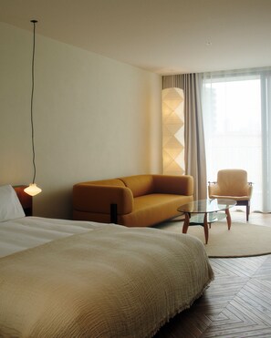 A hotel room with a bed, a sofa, a chair, a glass table, and a lamp. - MIZUTANI (Tokyo)