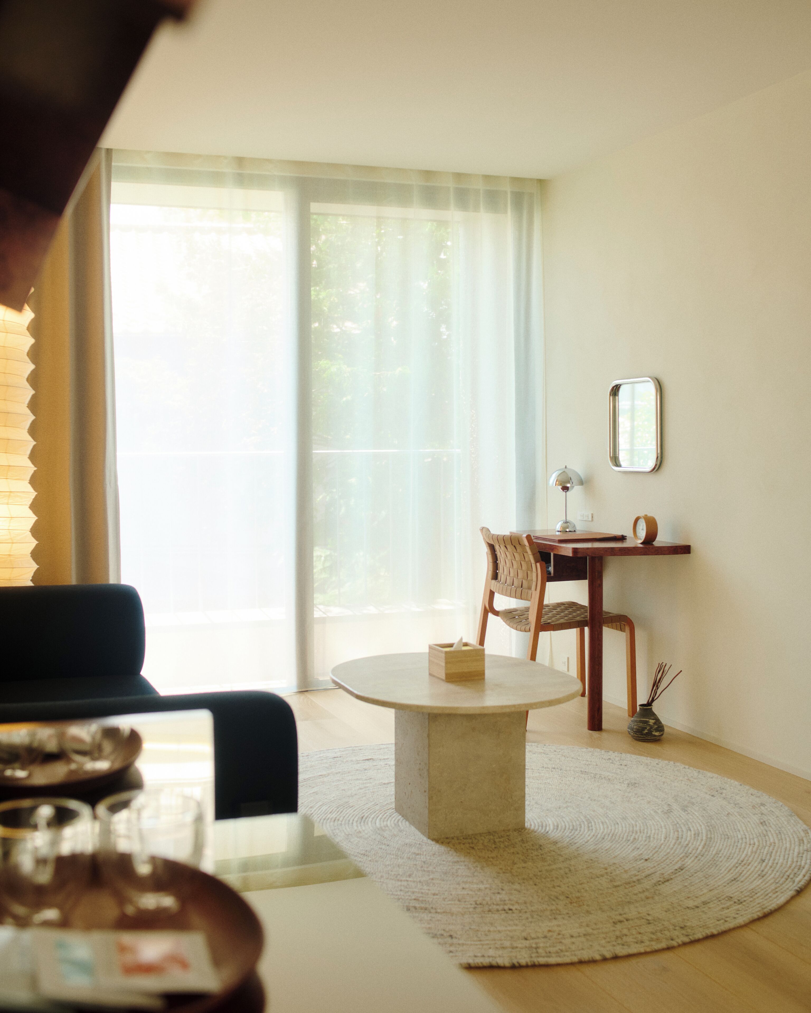 Une pièce avec une table ronde, une chaise, une petite table avec une lampe et une fenêtre avec des rideaux.