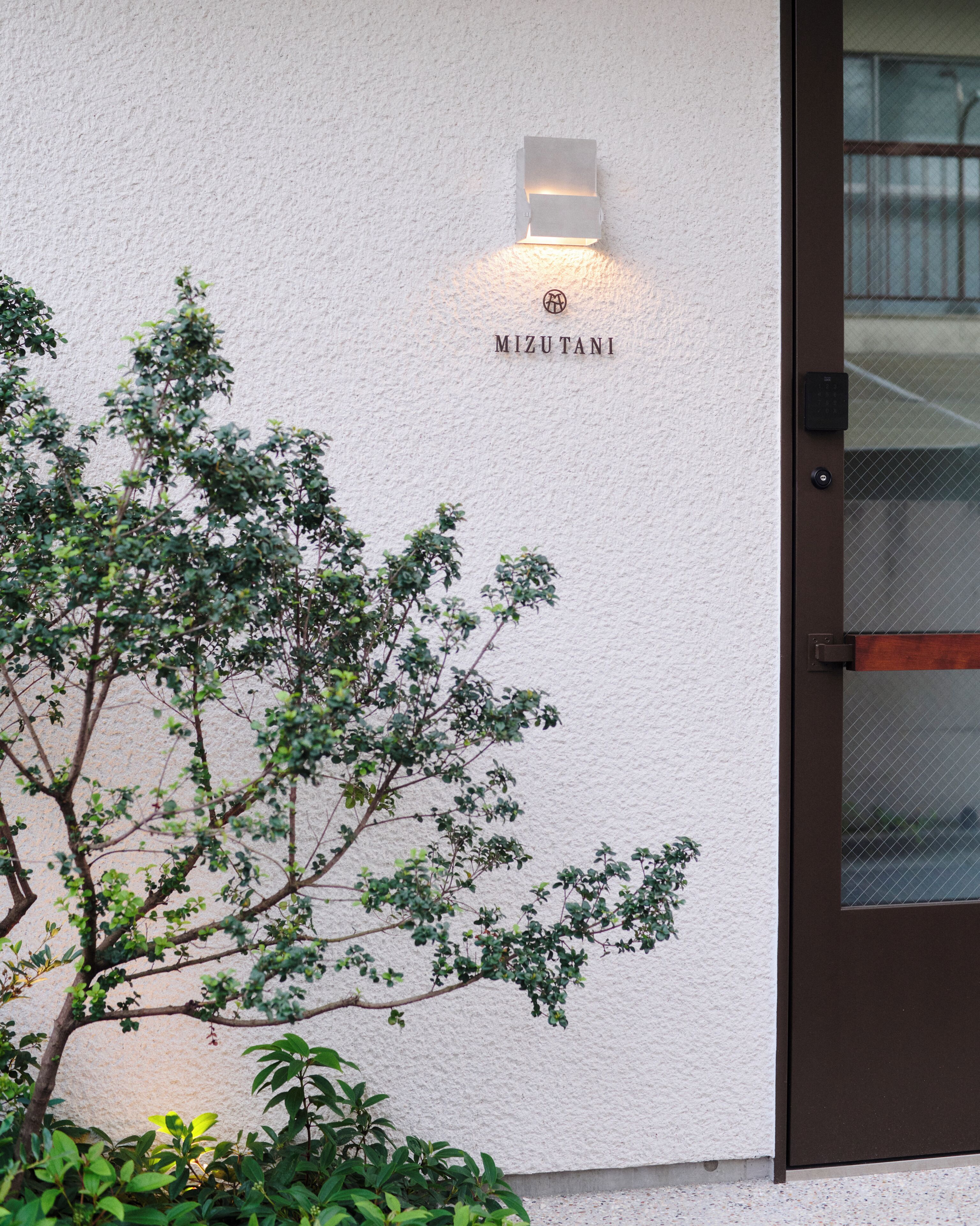 Une entrée d’immeuble avec une enseigne portant le nom « MIZUTANI » et une porte dotée d’un clavier de sécurité.