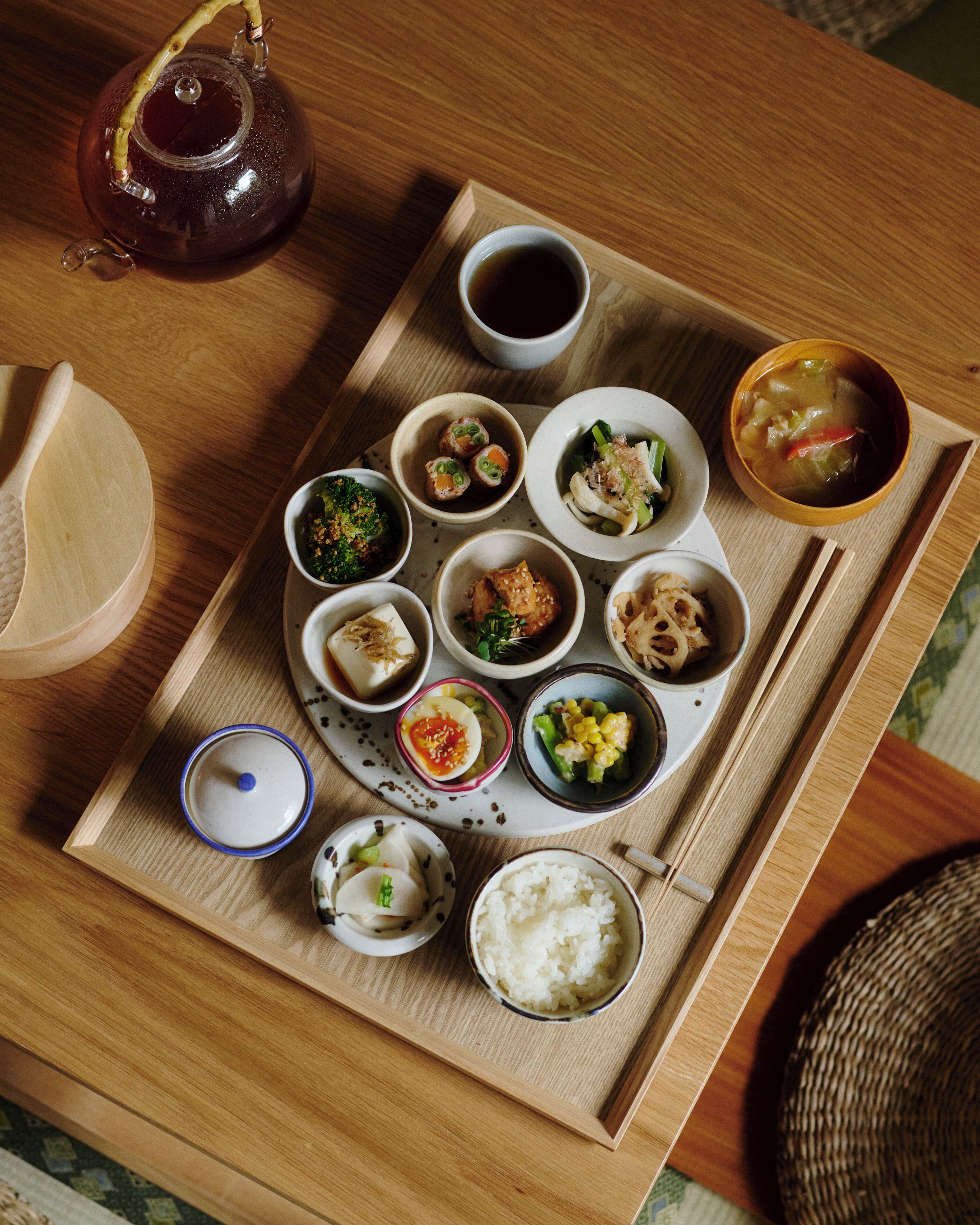 A wooden tray with various dishes and a teapot, suggesting a meal setting.