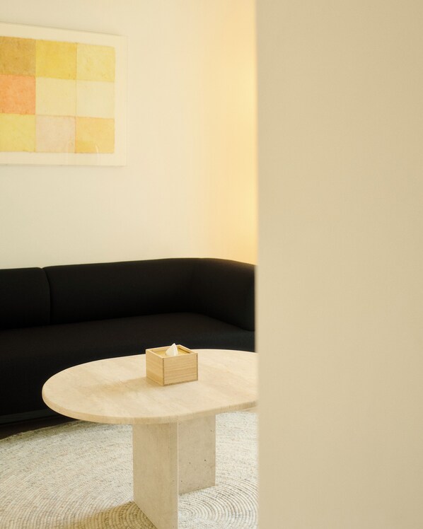 A room with a black sofa, a round table with a wooden box on it, and a textured rug.