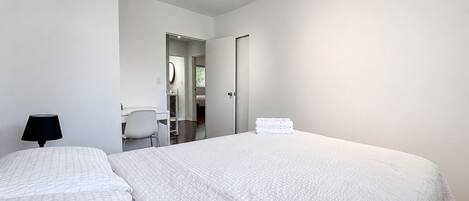 A modern bedroom with two beds, a desk, and a chair.