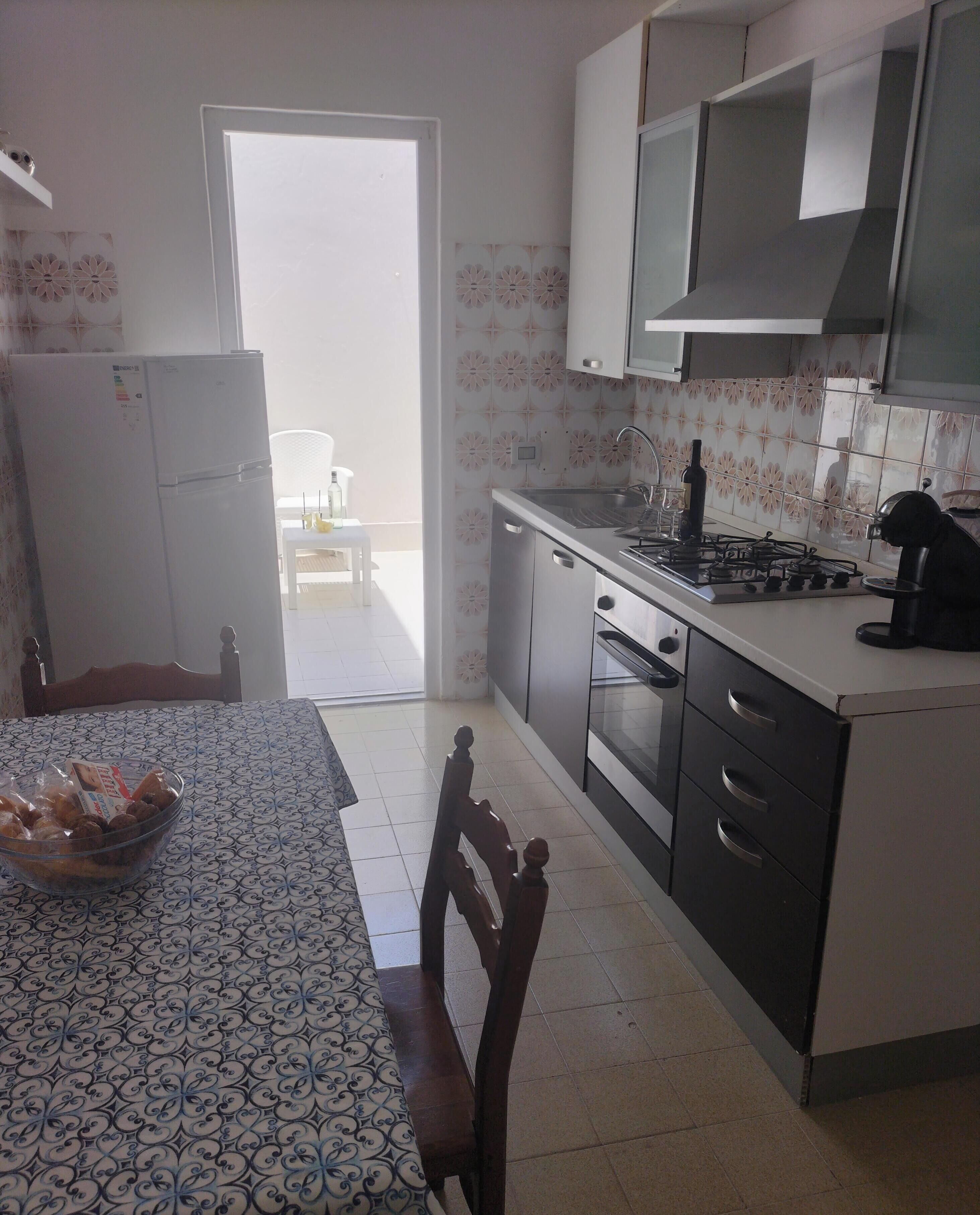 Uma cozinha com geladeira, fogão, forno e uma mesa de jantar com cadeiras.