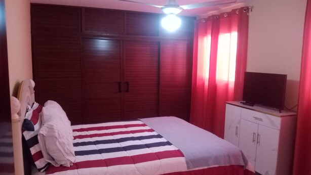 Ein Schlafzimmer mit einem Bett, einem Fernseher auf einem Schrank, einem Deckenventilator und roten Vorhängen.
