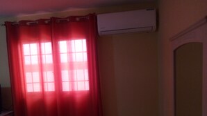 Ein Zimmer mit einem Fenster, das rote Vorhänge hat, einer an der Wand befestigten Klimaanlage und einer Tür mit einem Spiegel.