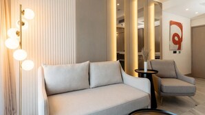 A modern living room with a sofa, armchair, and a round table with a vase.