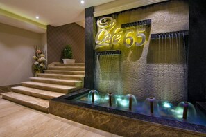 A hotel lobby with a staircase, a water feature, and a neon sign reading 'Café 65'. - The India Benares (Varanasi)