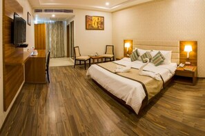 A hotel room with a large bed, a desk, a television, and a painting on the wall. - The India Benares (Varanasi)