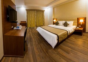 Une chambre d’hôtel avec un lit, un bureau, une télévision et une fenêtre avec des rideaux.