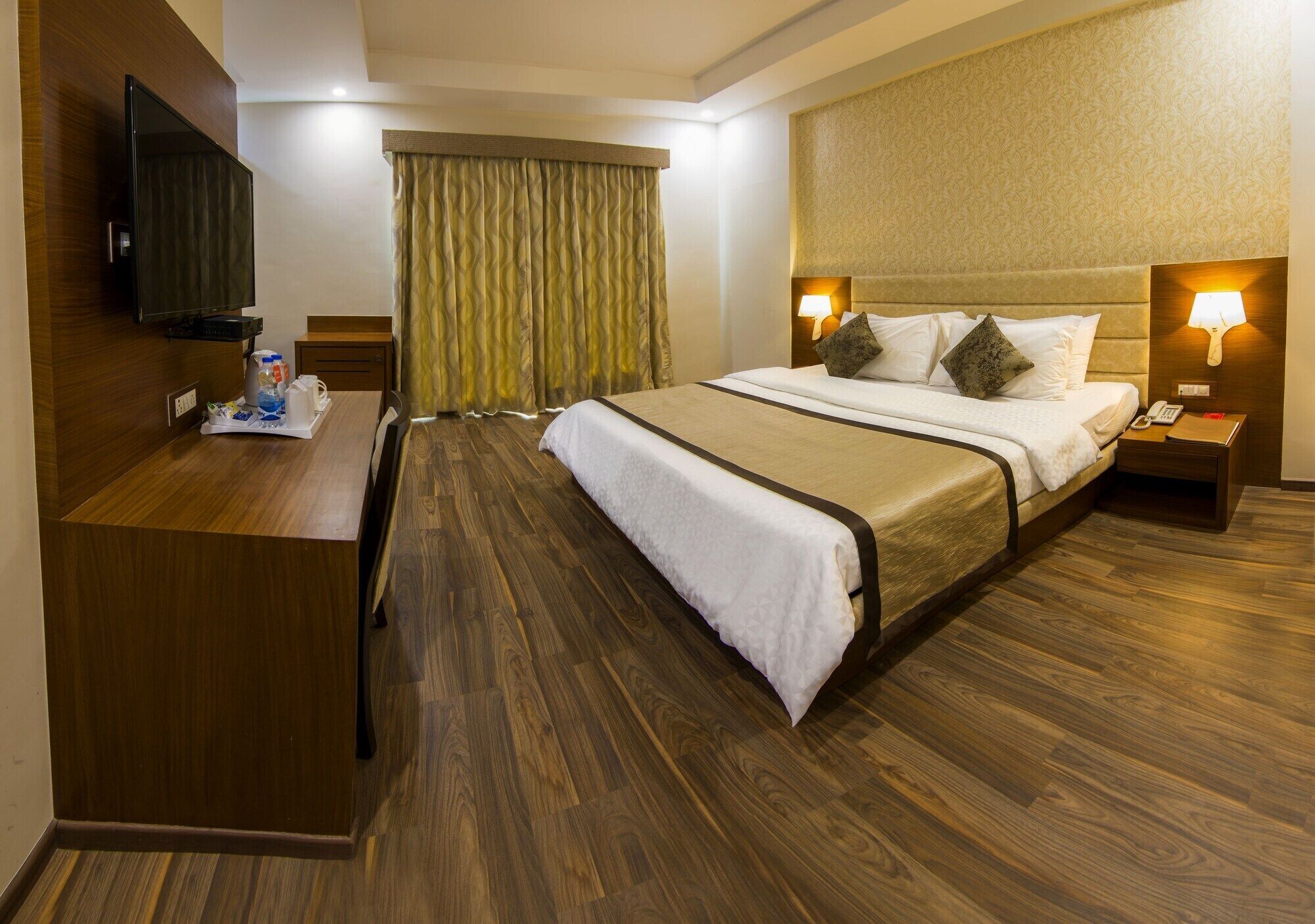 Habitación de hotel con cama, lámparas de noche, televisión, escritorio y suelo de madera.