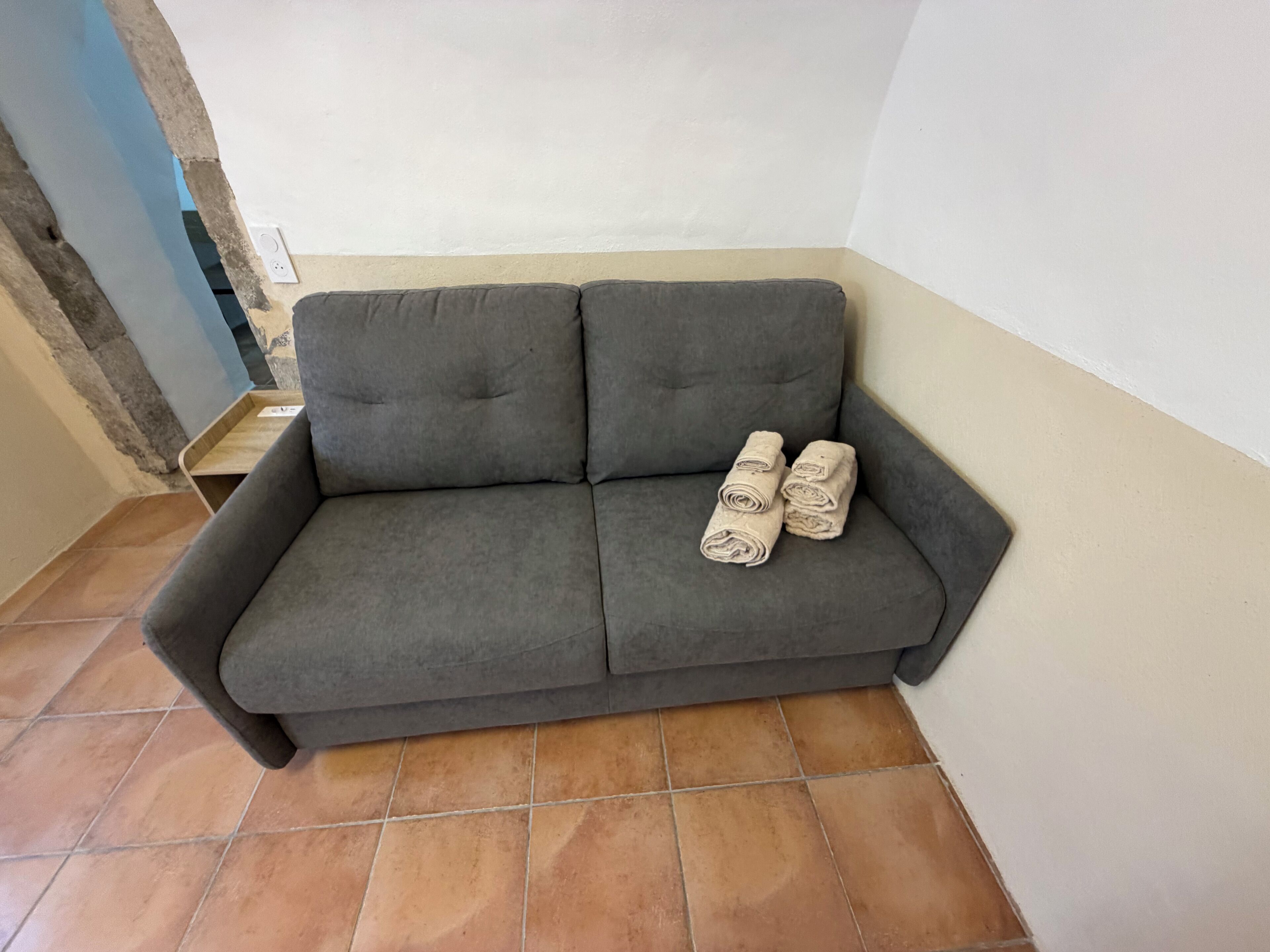 A grey sofa with rolled towels placed on it.