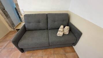 A grey sofa with rolled towels placed on it.