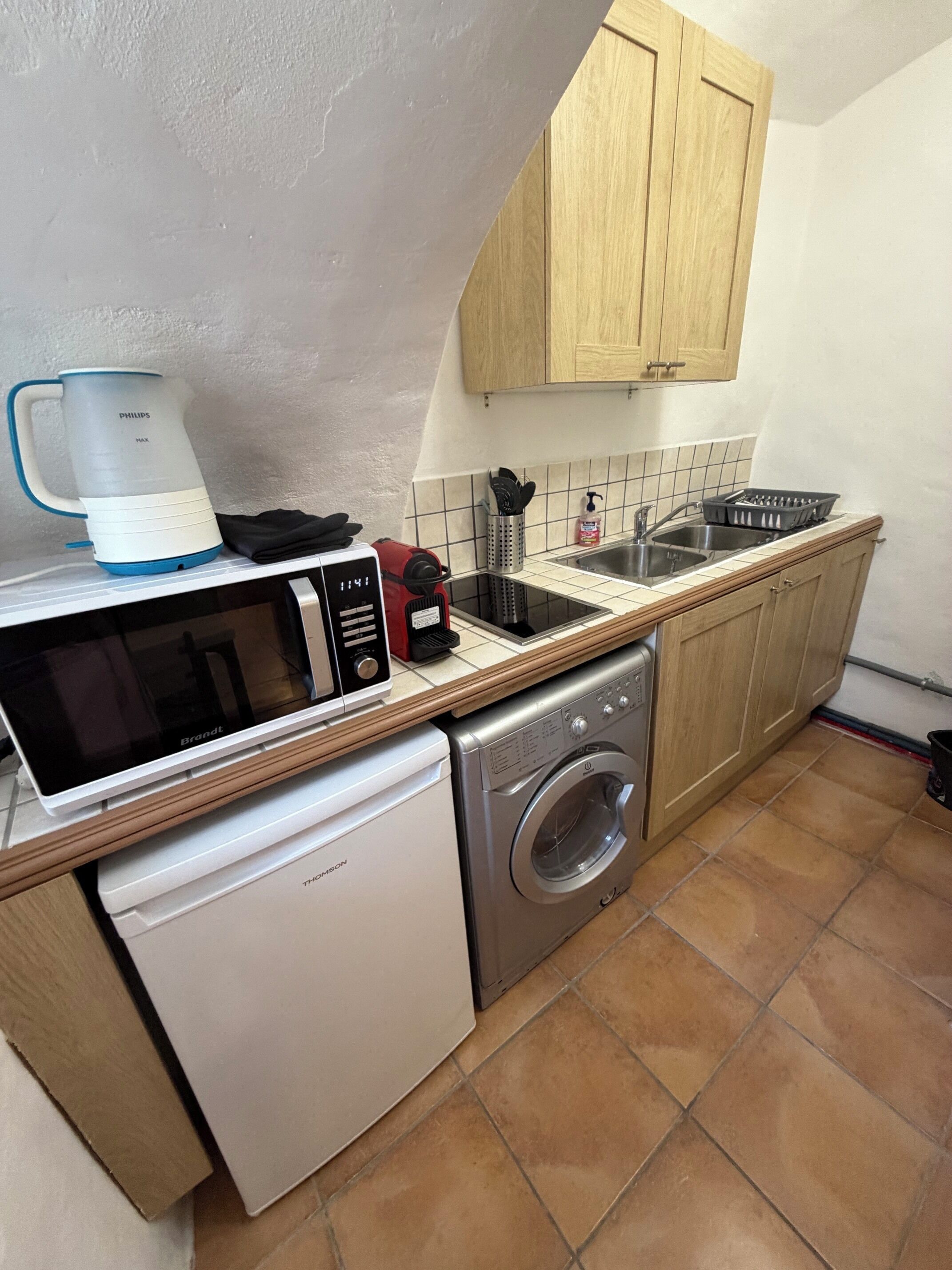 Een kleine keuken met een vaatwasser, magnetron, koffiezetapparaat en een wasmachine.