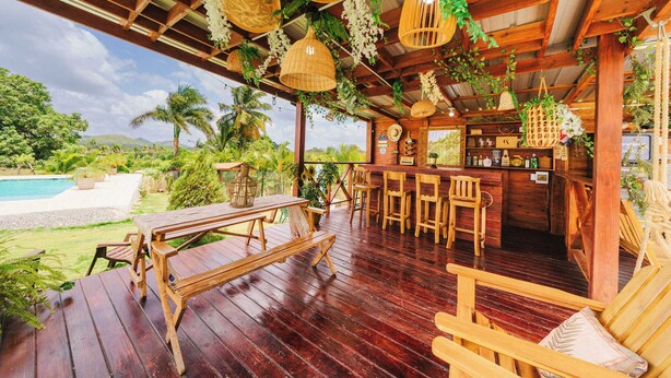 A wooden deck with a pool, outdoor seating, and a bar area. - Villa Campestre by Otium (Higuey)