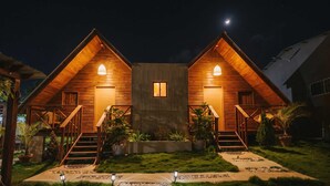 A two-story wooden cabin with a central window, surrounded by a well-maintained garden and a paved walkway. - Villa Campestre by Otium (Higuey)