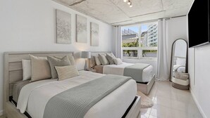 Ein modernes Schlafzimmer mit zwei Betten, einem großen Fenster mit Blick auf die Stadt, einem Flachbildfernseher und Kunstwerken an der Wand.
