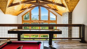 Una mesa de billar en una habitación con techo alto y ventanas grandes.