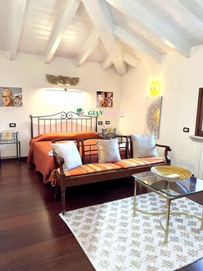 A bedroom with a bed, a sofa, a glass coffee table, a patterned rug, and a ceiling with exposed beams. - Villa on Pian degli olivi - Ref. Villa Eva-Rif. VillaEva (San Vincenzo)
