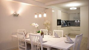 A modern dining area with white furniture, a vase of flowers, and a kitchen in the background. - Komfortable Auszeit in Winterberg (Winterberg)
