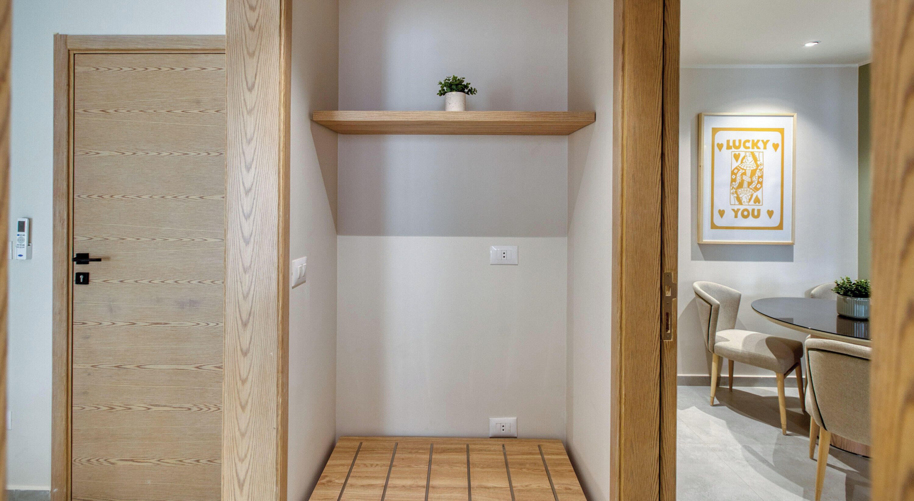 Un pasillo con una puerta de madera, un estante con una planta y un comedor con sillas y una mesa.