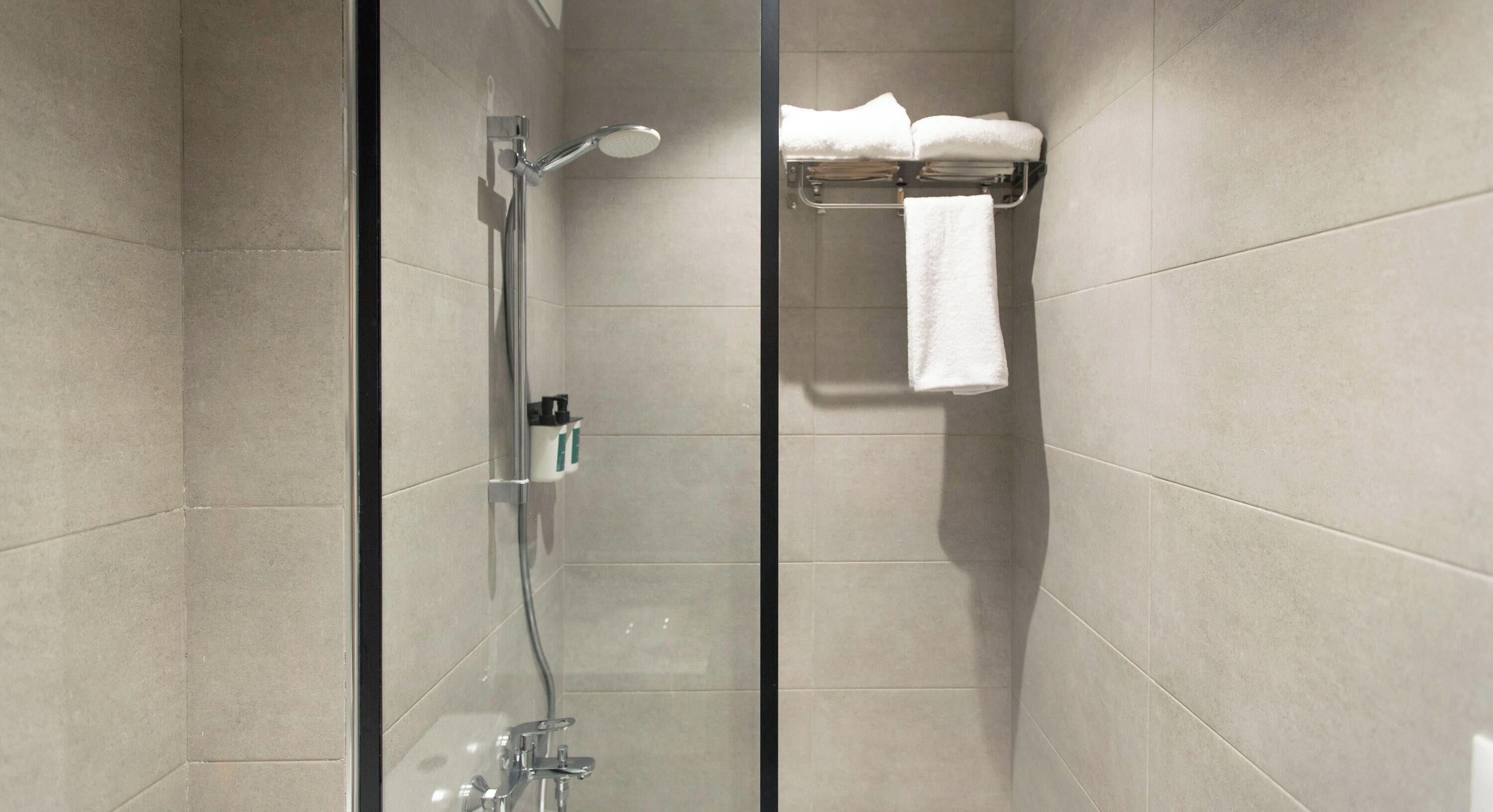 Um chuveiro moderno com porta de vidro, um porta-toalhas com toalhas dobradas e um suporte para pequenos frascos.