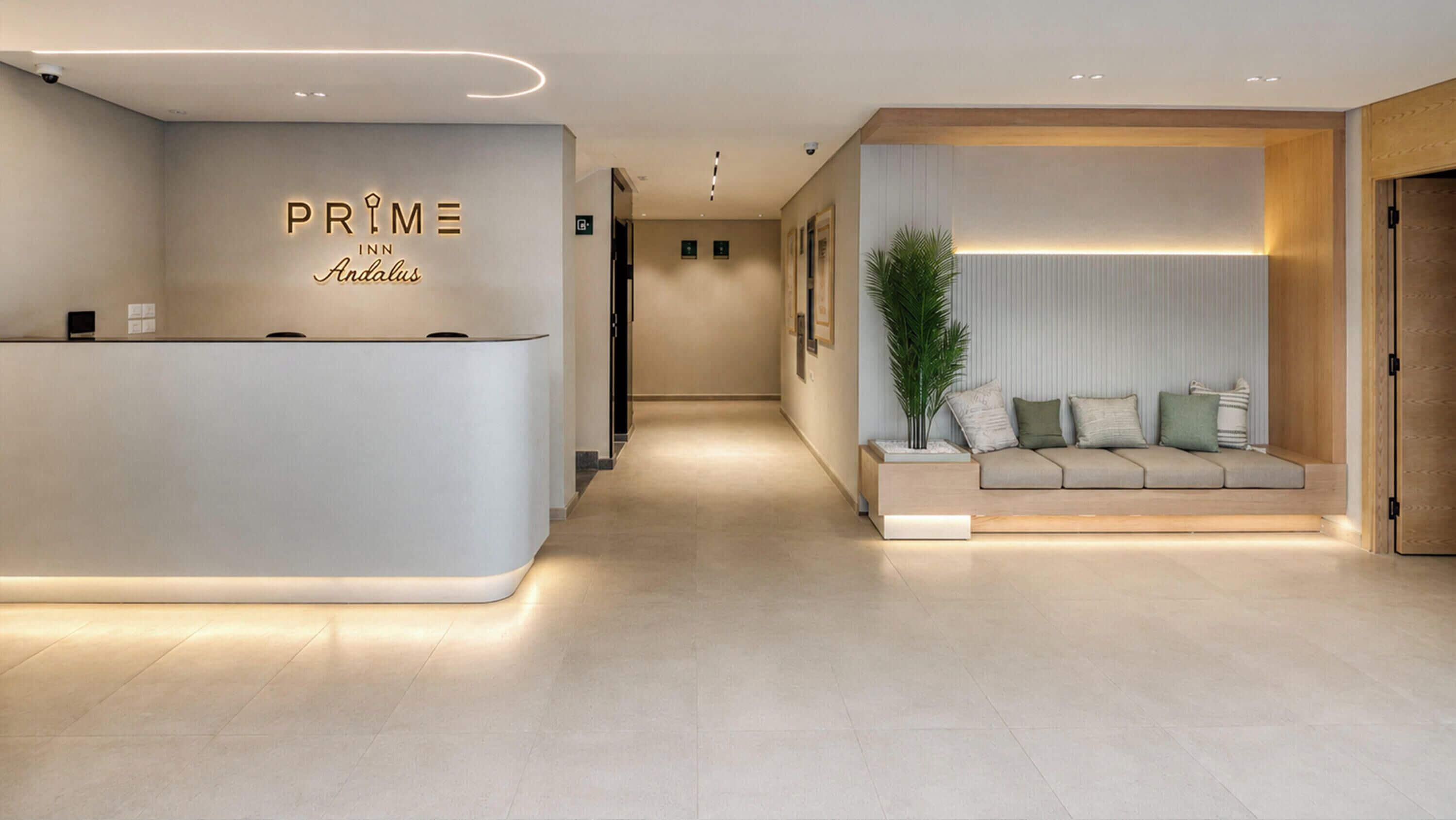 Zona de recepción de hotel con diseño moderno, una mesa de recepción, un área de estar con cojines y una planta en maceta.