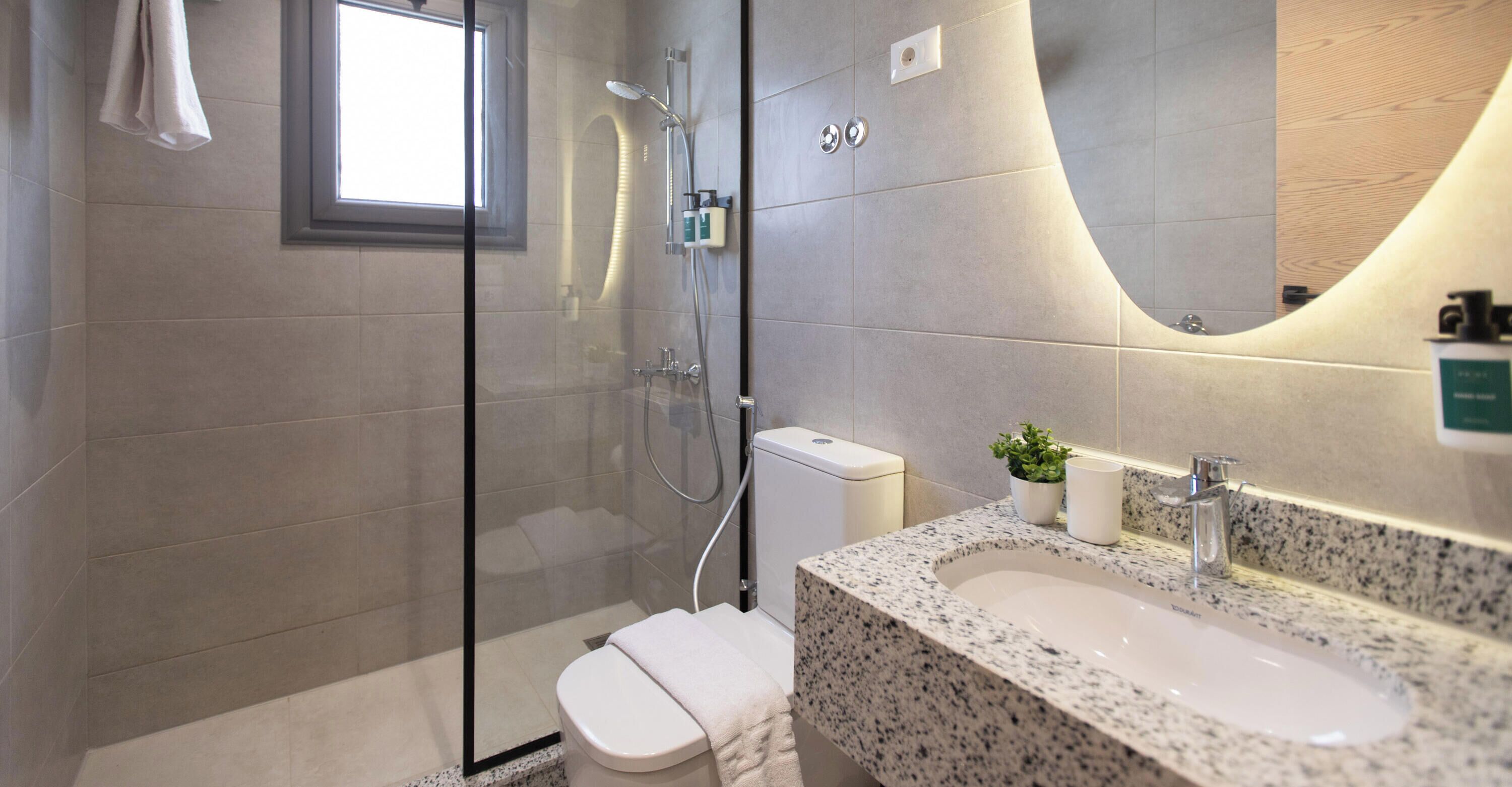 Een moderne badkamer met een glazen douchecabine, toilet, wastafel met een granieten blad en een spiegel die de ruimte weerspiegelt.