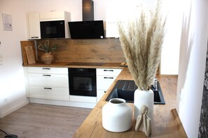 Eine moderne Küche mit weißen Schränken, einer Holz Arbeitsplatte, einer Mikrowelle und einer Vase mit Pampasgras.