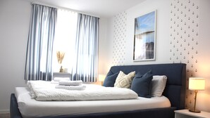 A neatly made bed with white linens, a dark blue headboard, and a bedside table with a lamp. - Semi-detached house - 4 bedrooms for families and friends (Jesendorf)