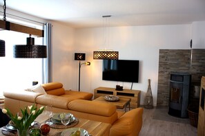 Ein modernes Wohnzimmer mit einer Sofagarnitur, einem Flachbildfernseher, einem Kamin und einem Essbereich mit Tisch für zwei Personen.