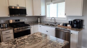 A kitchen with white cabinets, a stainless steel stove, a granite countertop, a sink, and a coffee maker.