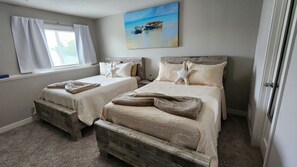 A bedroom with two beds, a window with curtains, a painting of boats on the wall, and a starfish decoration.