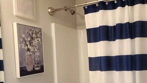 Ein Badezimmer mit Toilette, Badewanne, Duschvorhang, Lüftung und einer Vase mit Blumen auf der Ablagefläche.