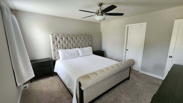 A bedroom with a bed, a nightstand, a ceiling fan, and a door.