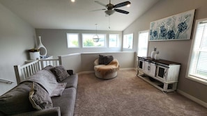A room with a gray sofa, a round chair, a white cabinet, and a ceiling fan.