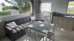 A compact living space with a sofa, dining table, chairs, a kitchen area, and large windows. - Mobile Home, at a Campground ⭐️⭐️⭐️⭐️⭐️ 3 km from the ocean (Saint-Arnoult)