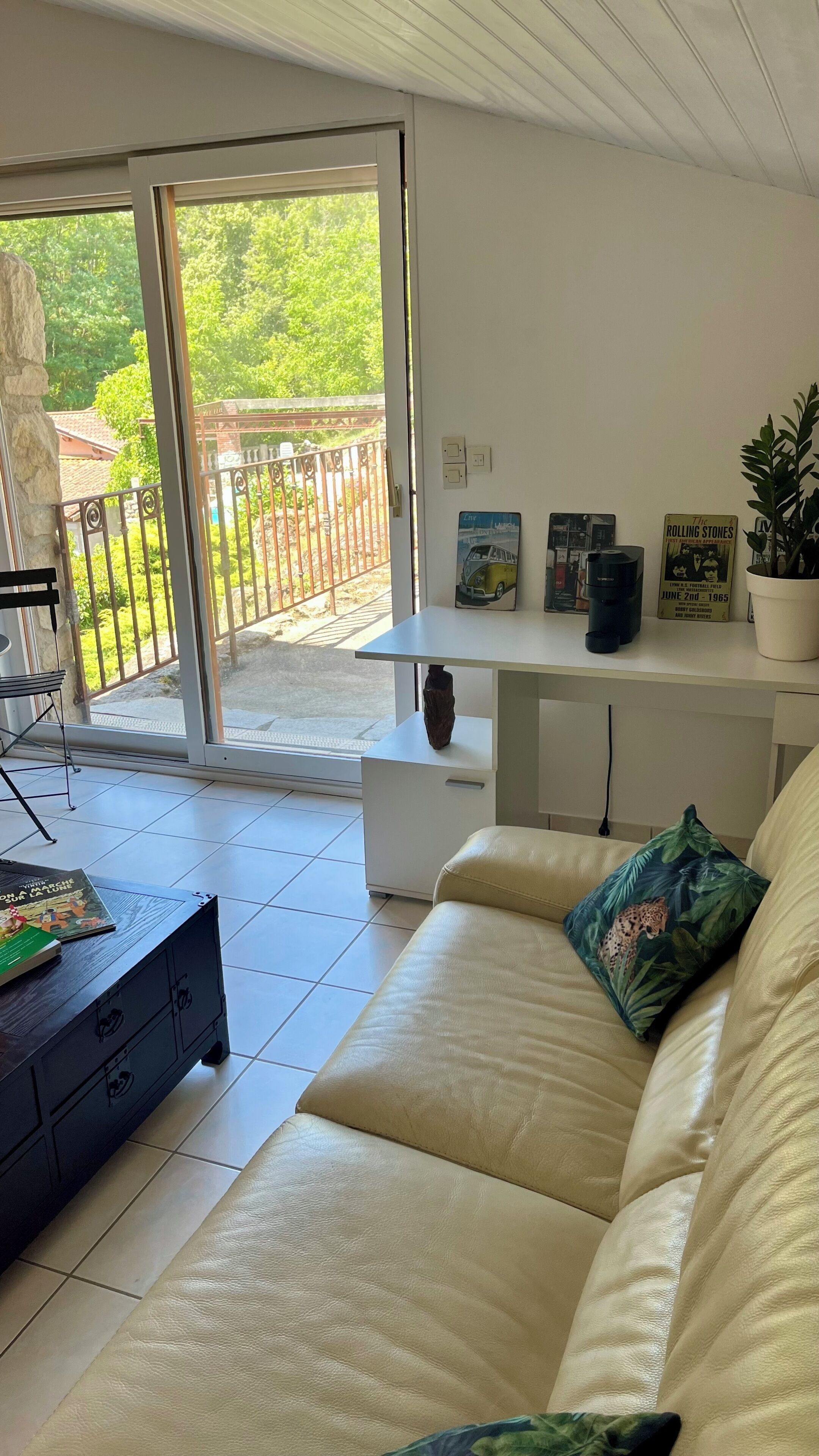 A living room with a sofa, a coffee table, and a bookshelf. There is a sliding glass door leading to an outdoor area with a balcony.