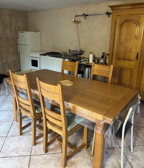 A dining area with a wooden table, chairs, a kitchen in the background, and a wooden cabinet.