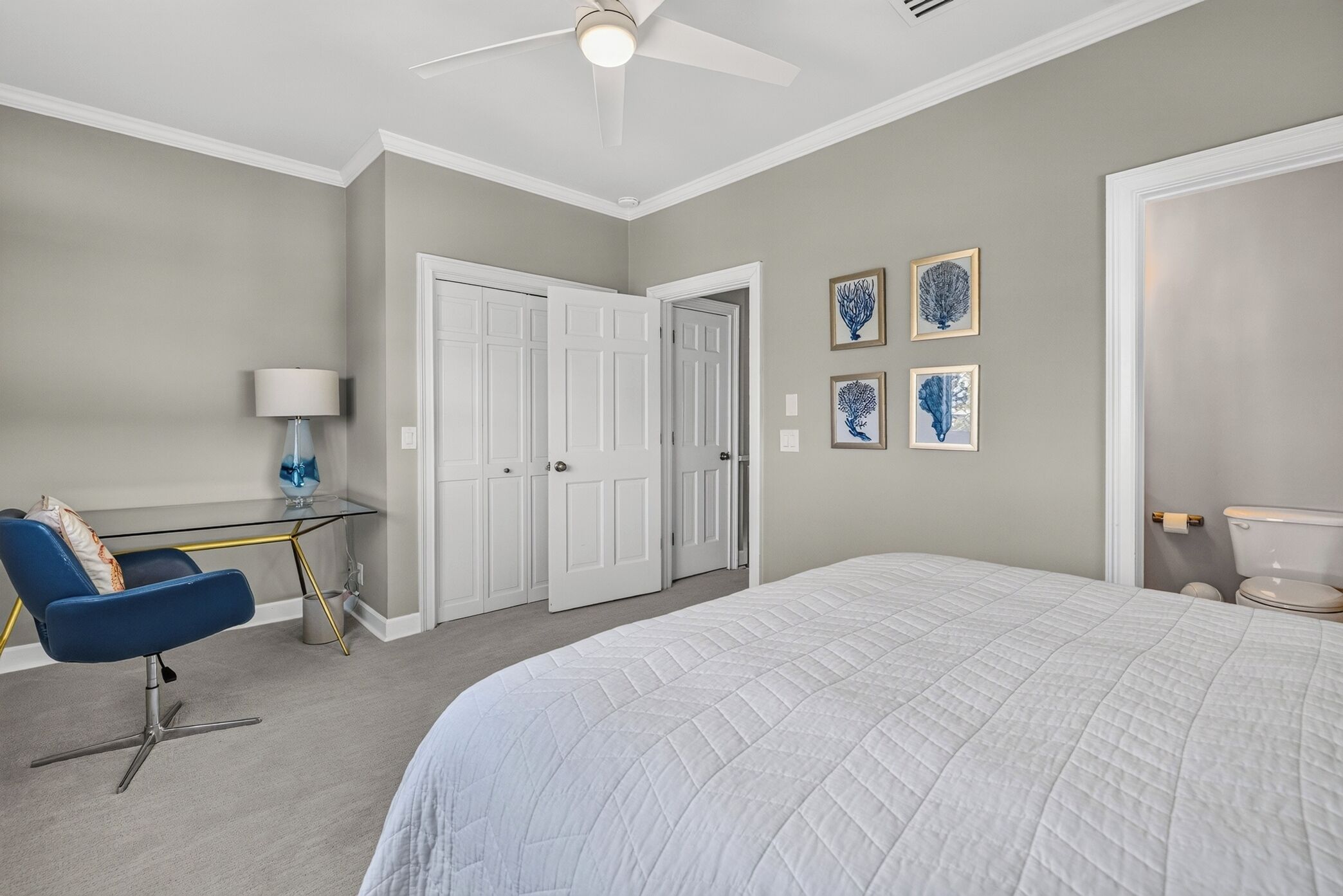 A bedroom with a bed, a desk, a chair, a ceiling fan, and a door.