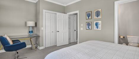 A bedroom with a bed, a desk, a chair, a ceiling fan, and a door.