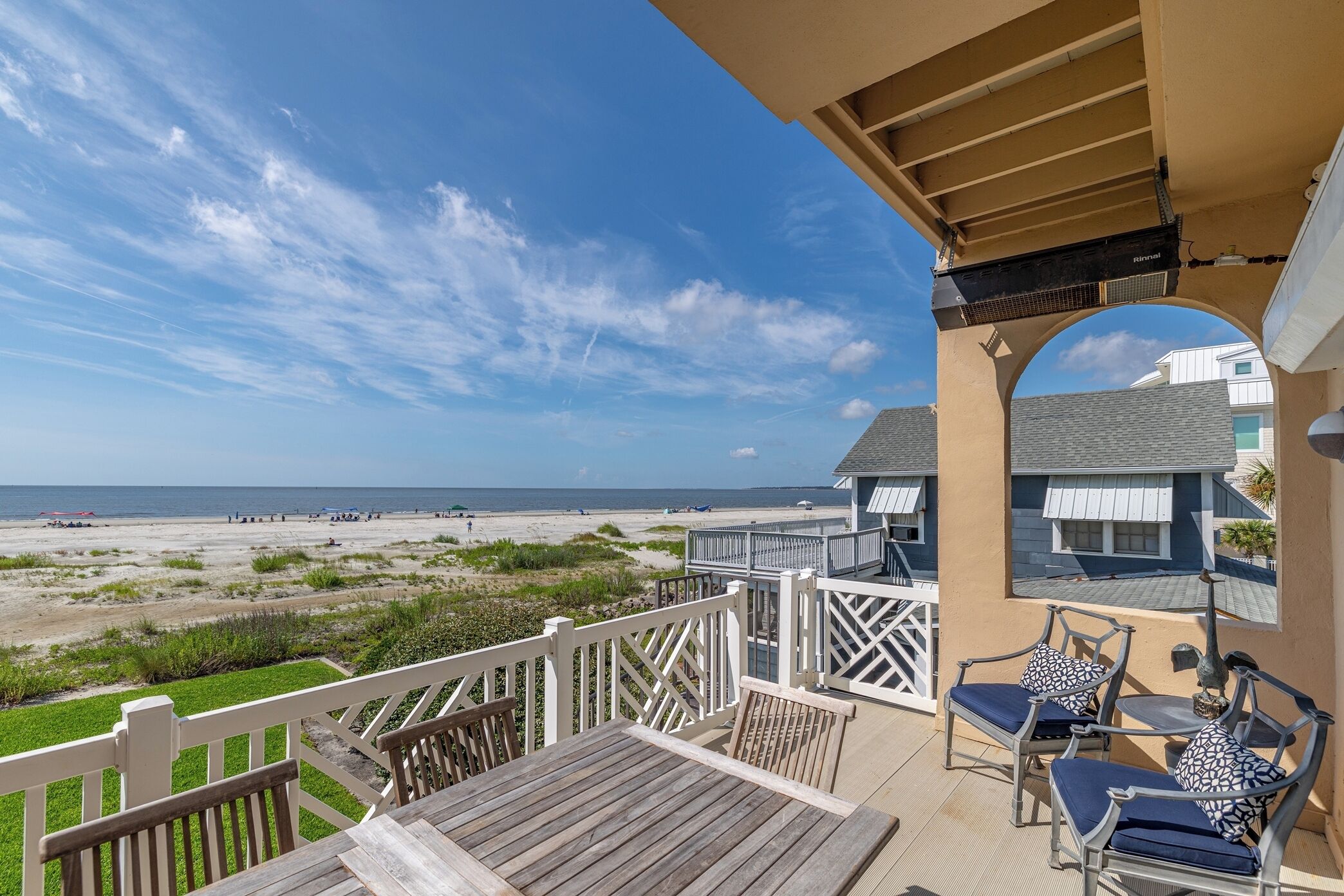 A balcony with a view of the beach, a wooden table, and two chairs.