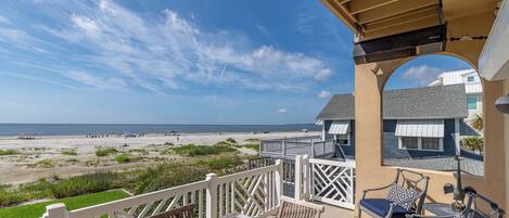 A balcony with a view of the beach, a wooden table, and two chairs.
