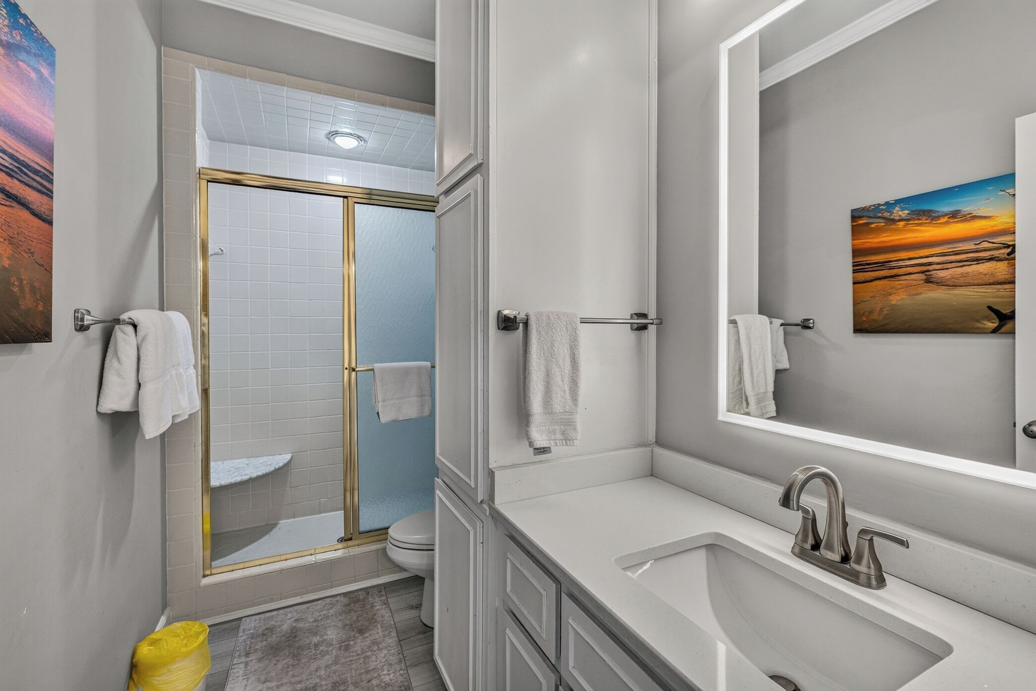 A bathroom with a shower, a sink, a mirror, and a painting on the wall.