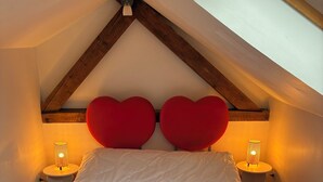 A bedroom with a sloped ceiling, a bed with a red upholstered headboard, two bedside lamps, and a wooden floor.