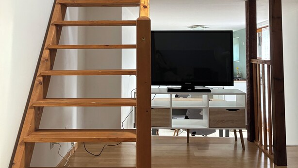 A wooden staircase leading to a loft bedroom with a TV in the living area.